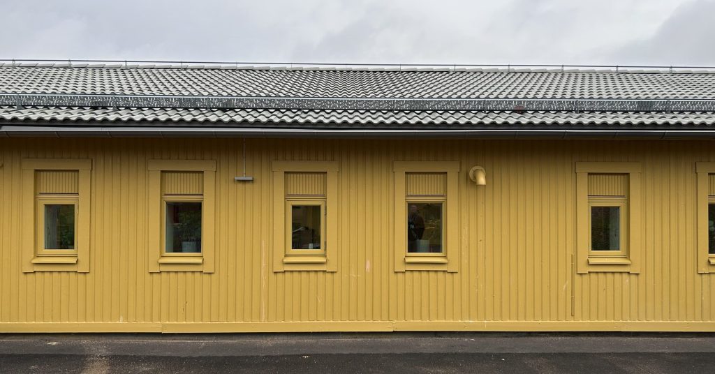 Gul enplansbyggnad med träfasad och små fönster.